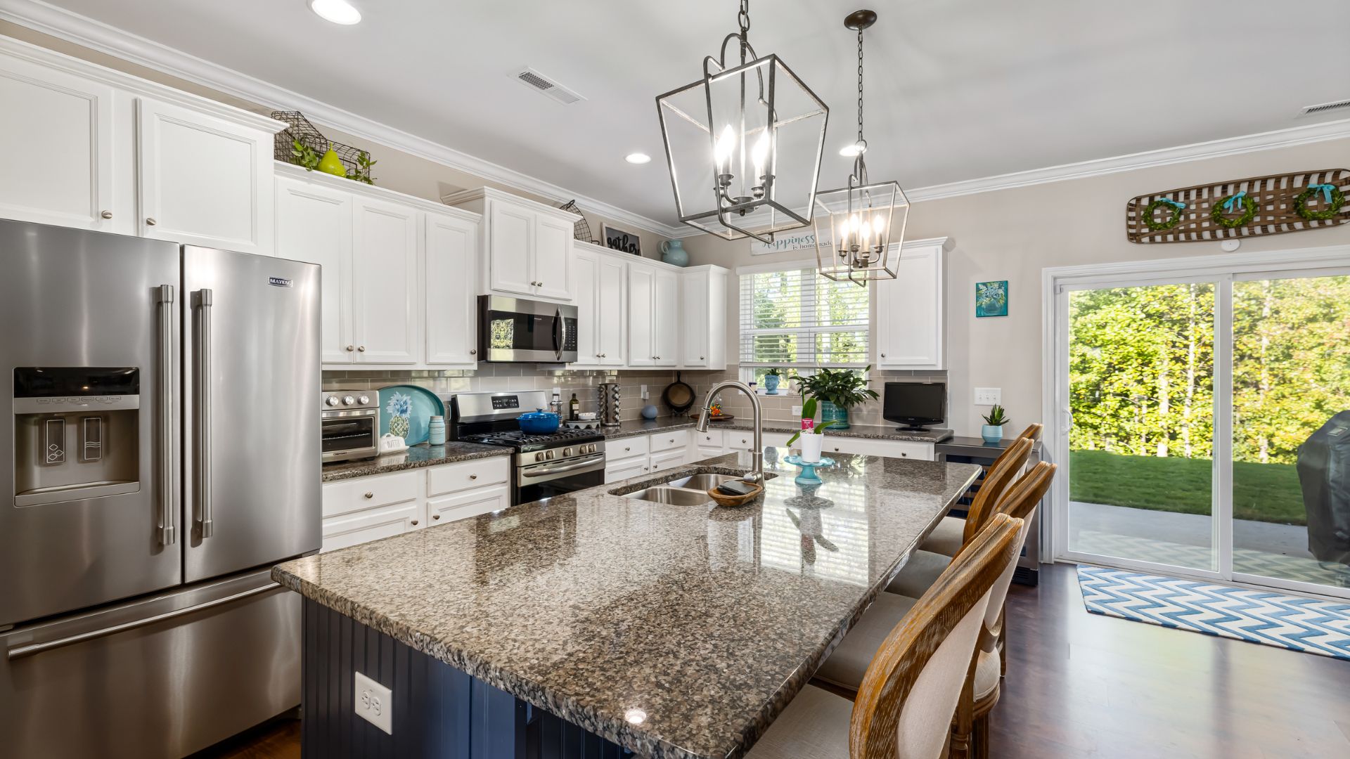 Modern white kitchen with granite island, stainless appliances, and garden view
