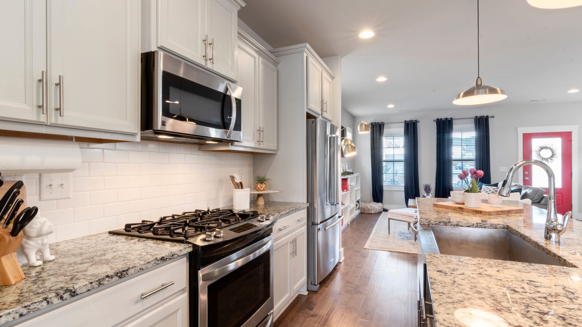 Modern white kitchen with granite countertops, stainless steel appliances, and hardwood floor