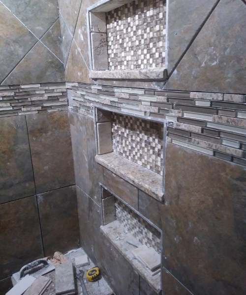 Tiled shower with three built-in stone shelves and mosaic tile accents