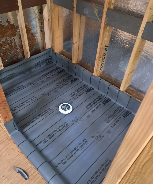 Shower base with waterproofing membrane and drain installed during bathroom renovation