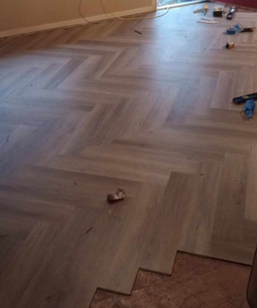 Herringbone wood flooring installation in progress with tools scattered around