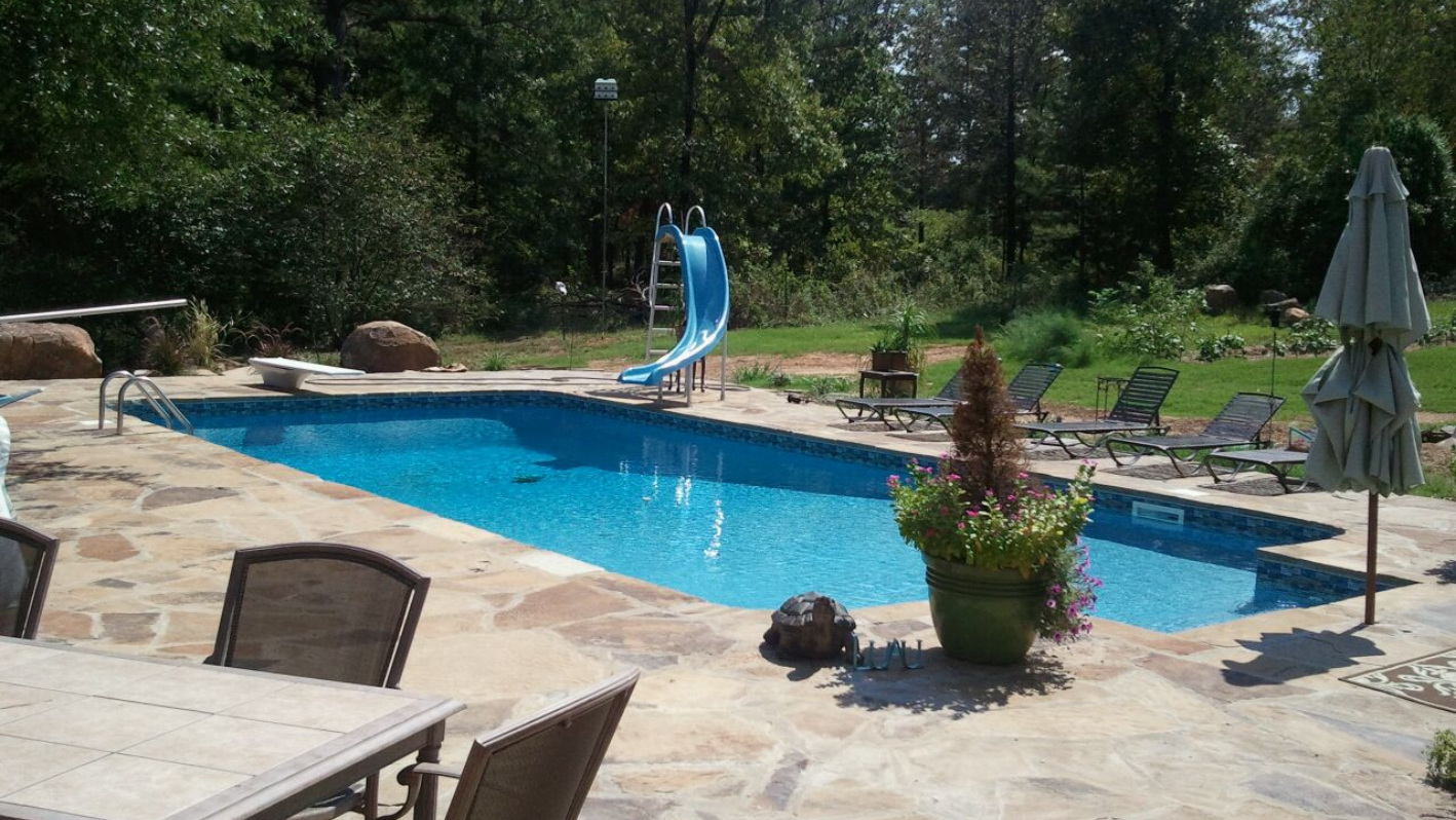 Backyard swimming pool with blue slide, lounge chairs, and stone patio