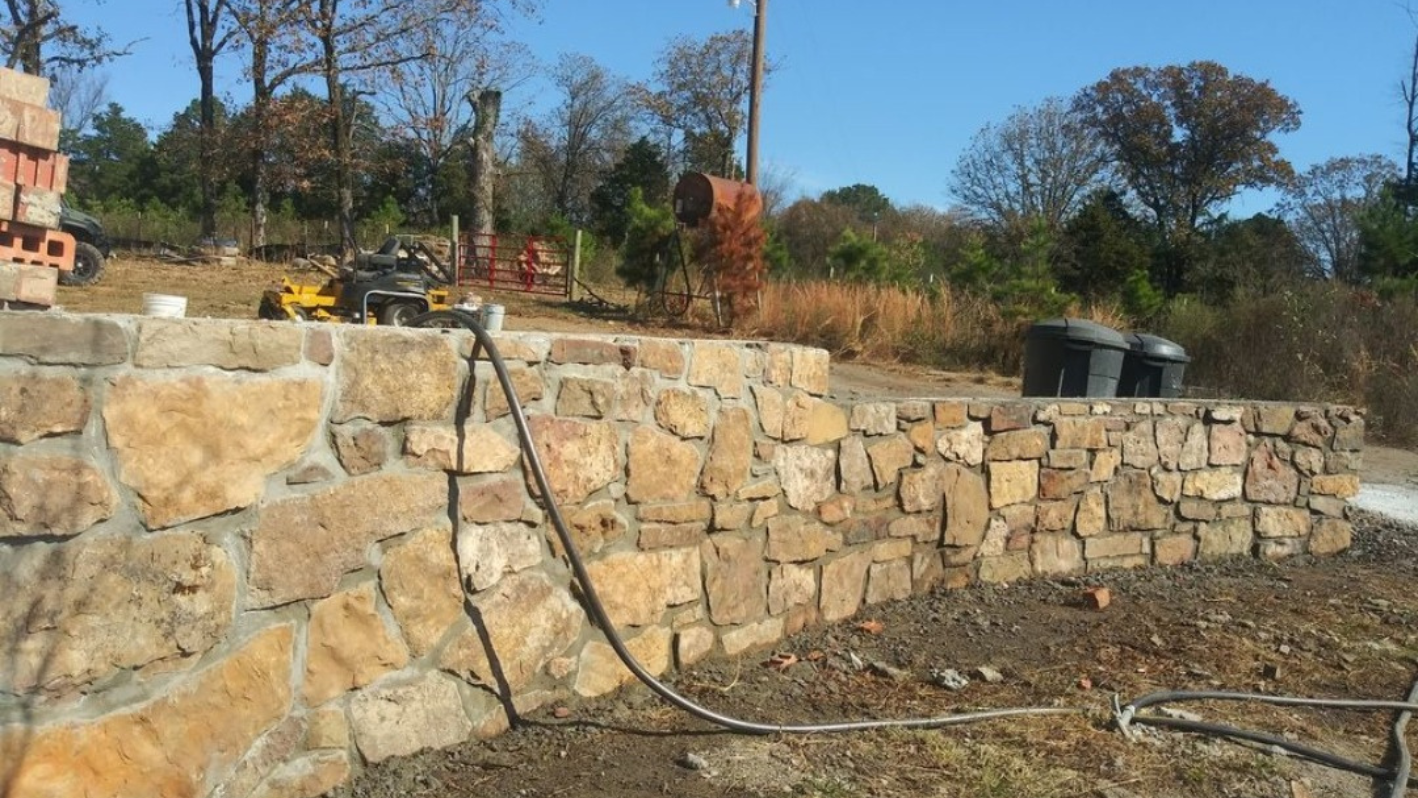 Stone retaining wall under construction with equipment in rural landscape